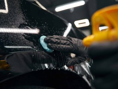 Cropped photo of skilled worker in nitrile gloves pressing lump of clay to car surface